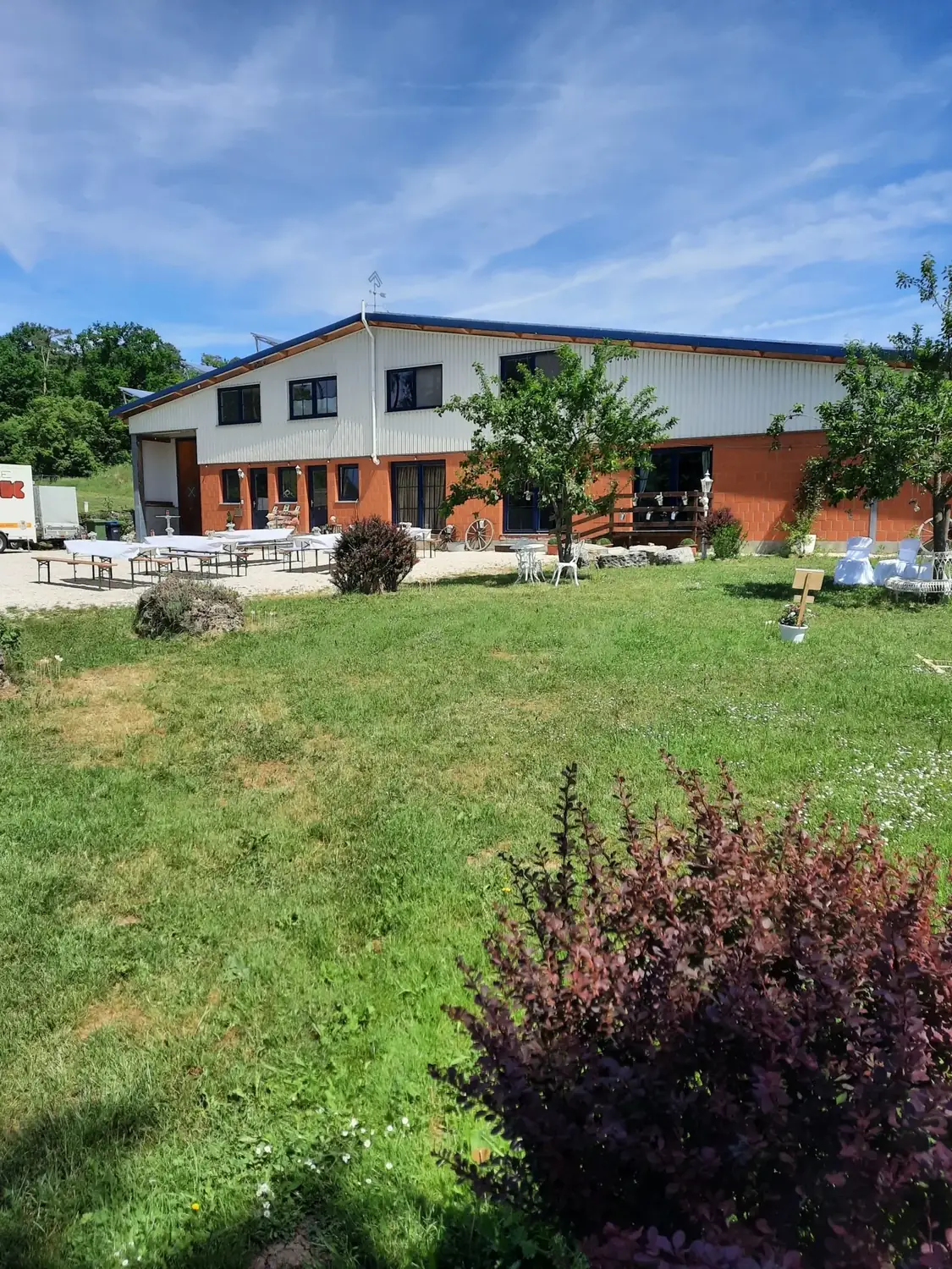 Blick über die Gartenwiese auf das Hauptgebäude mit Biertischen und weißen Gartenstühlen