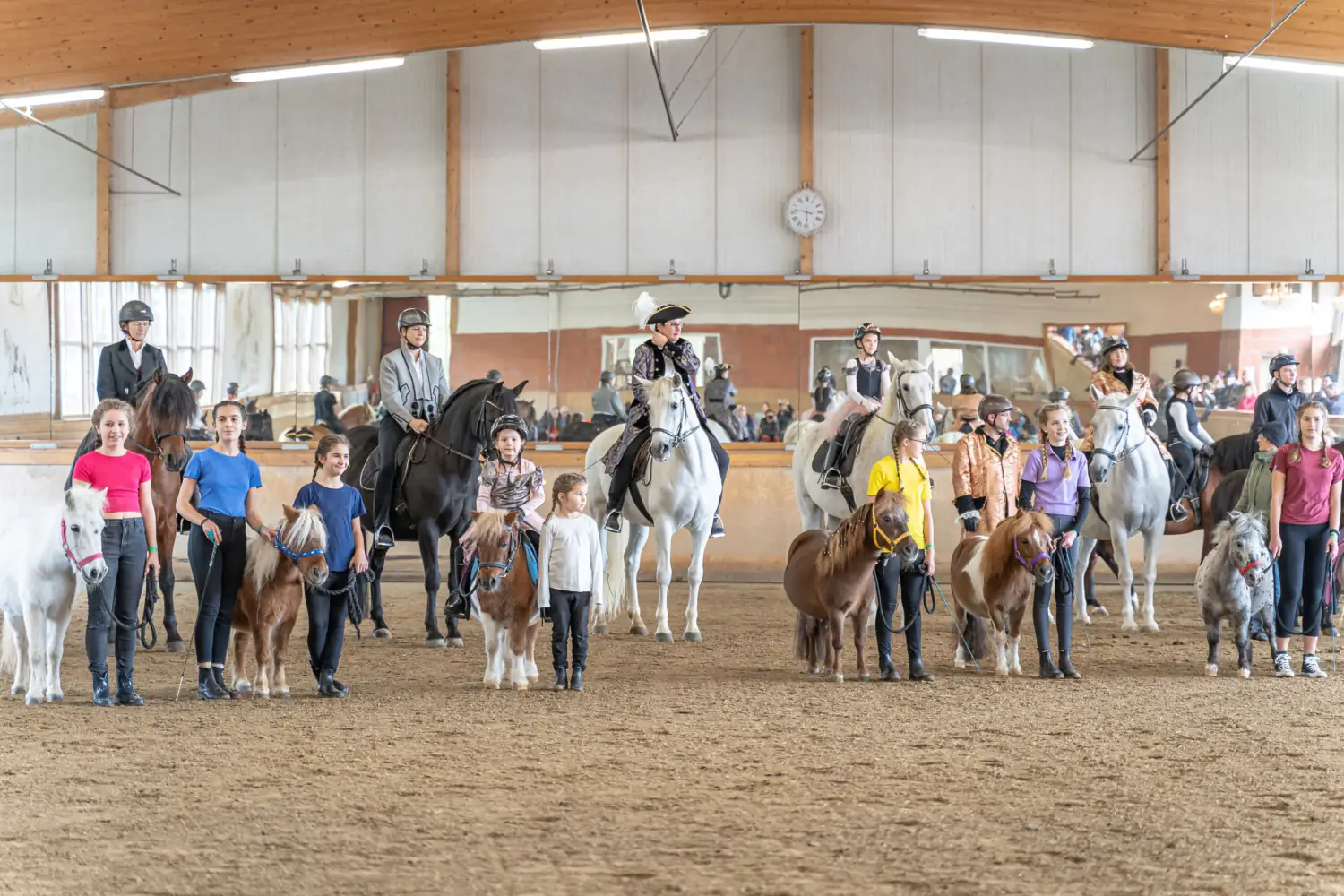 Kinder mit Ponys an der Hand und Reiterinnen zu Pferd stehen nebeneinander in der Reithalle