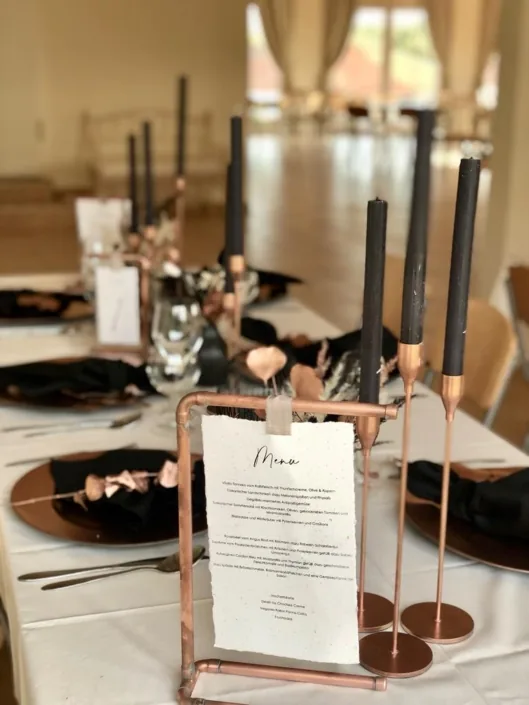 Menükarte in einem Kupferständer auf einer weiß gedeckten Tafel mit schwarzen Kerzen