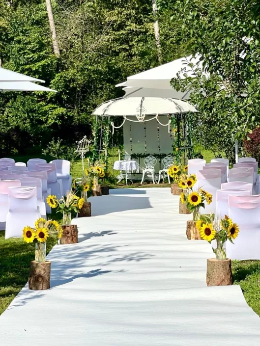 Weißer Teppich führt zwischen Stuhlreihen und Sonnenblumen zu einem Pavillon im Garten