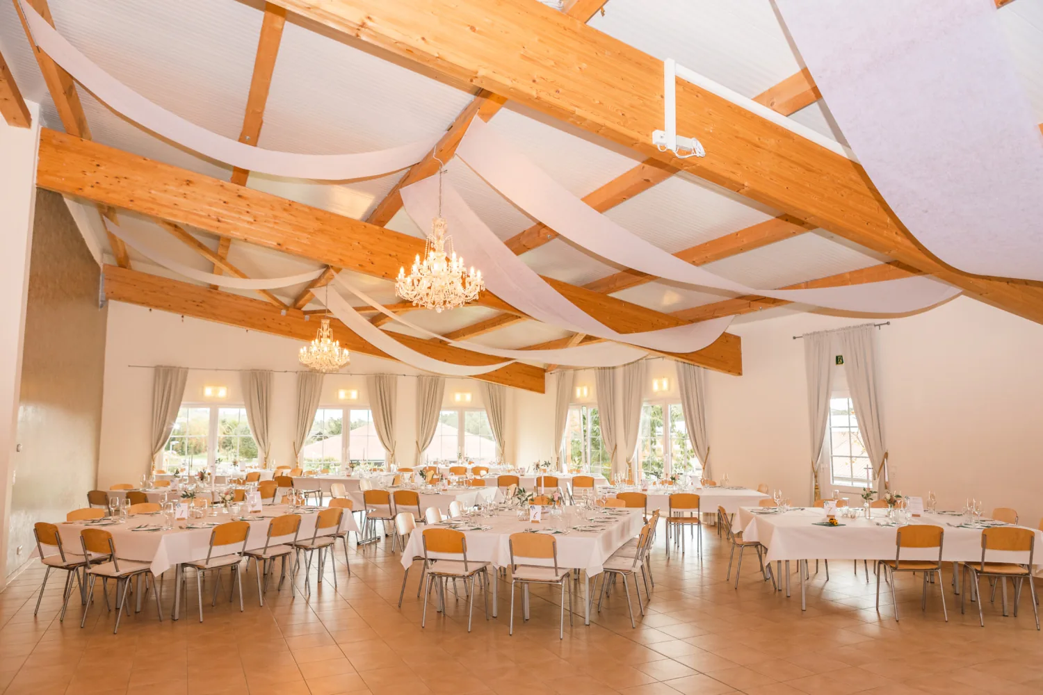 Festsaal mit offenem Holzdachstuhl, zwei Kronleuchtern und langen gedeckten Tafeln