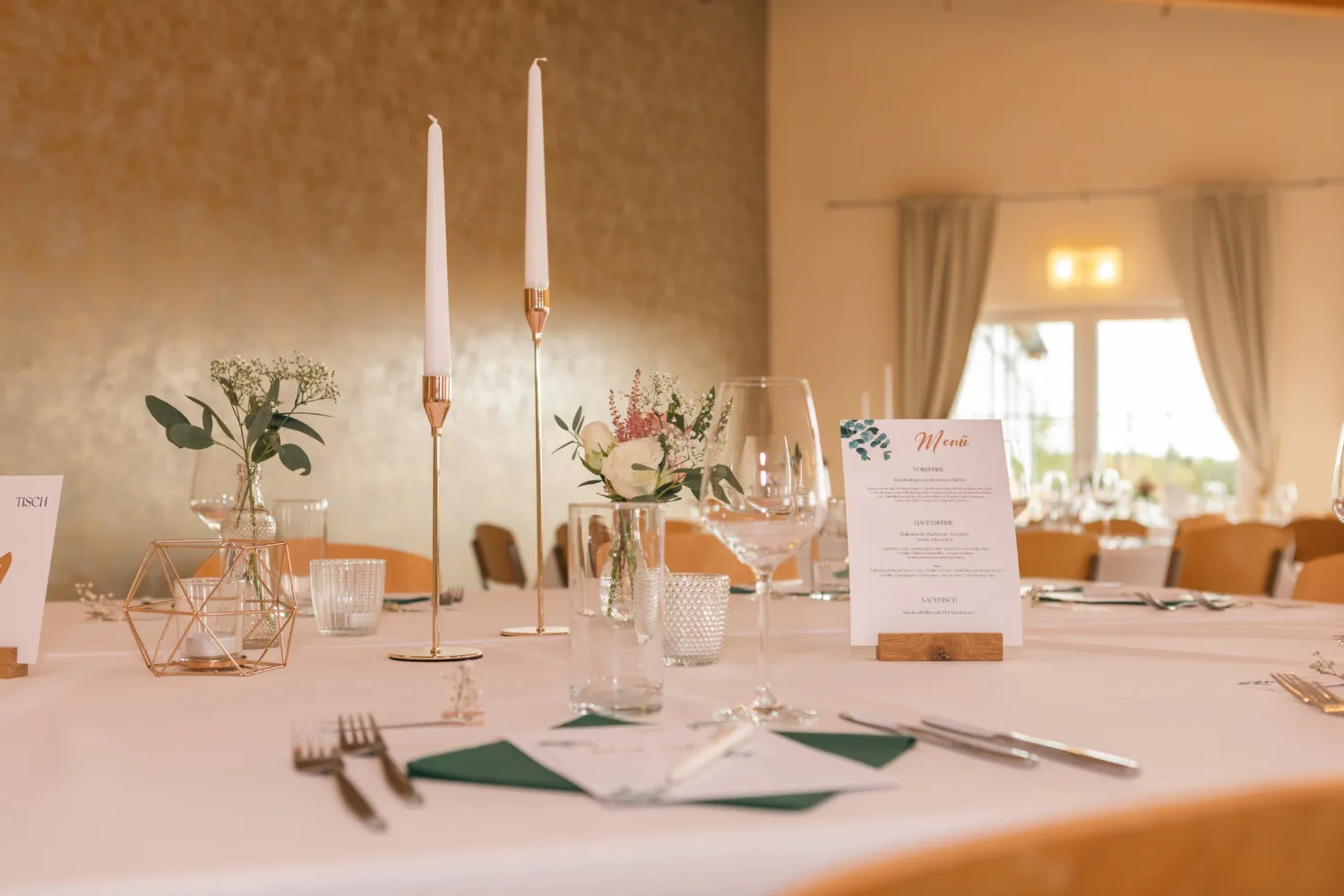 Gedeckter Tisch mit Menükarte, schmalen Messingleuchtern, grünen Servietten und Eukalyptus in kleinen Vasen