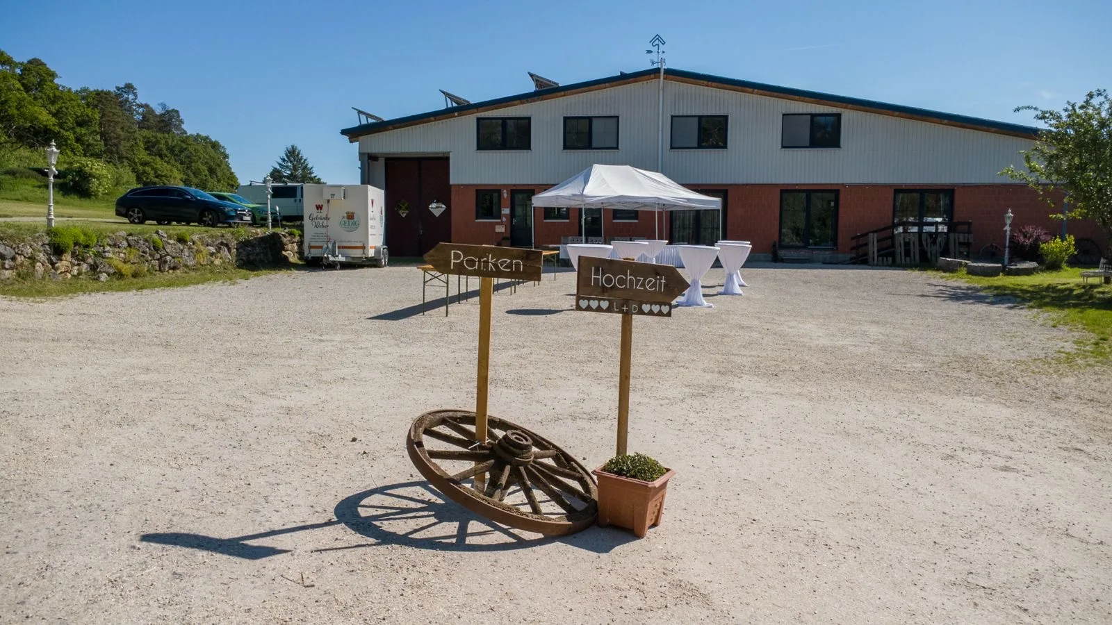 Hölzerner Wegweiser mit den Schildern „Parken“ und „Hochzeit“ neben einem alten Wagenrad auf dem Hofplatz