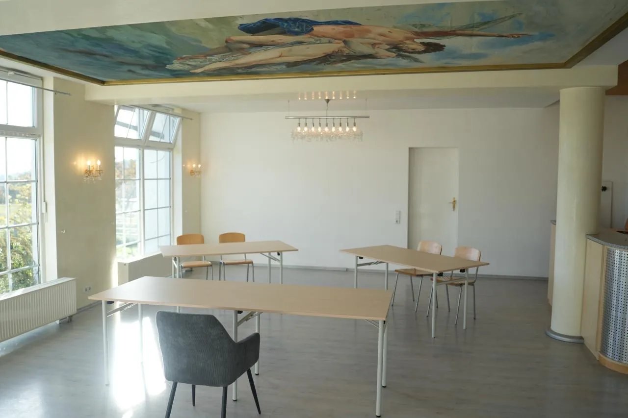 Raum mit gemaltem Deckenbild, Kristallkronleuchter, heller Säule und Theke im Hintergrund