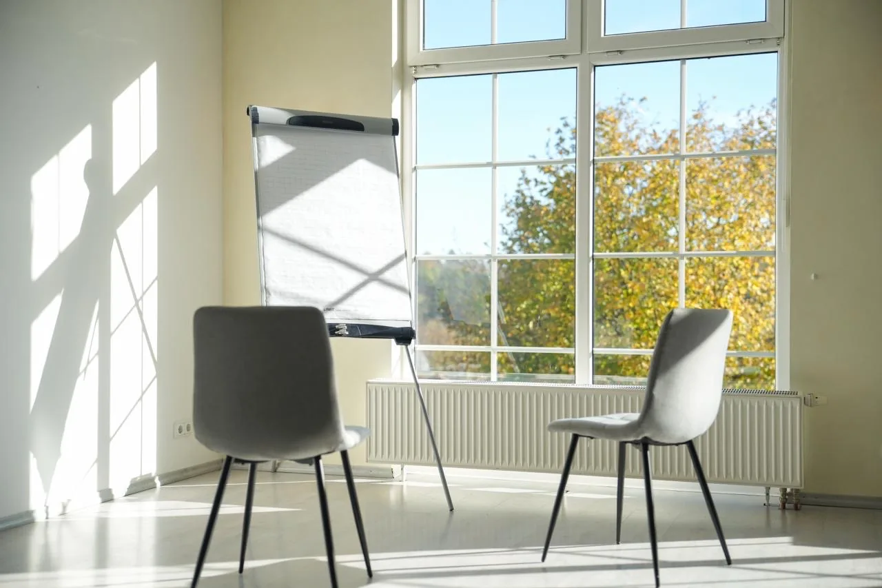 Flipchart mit zwei Stühlen vor dem hohen Sprossenfenster der Salle de Pluvinel, draußen ein herbstlicher Baum