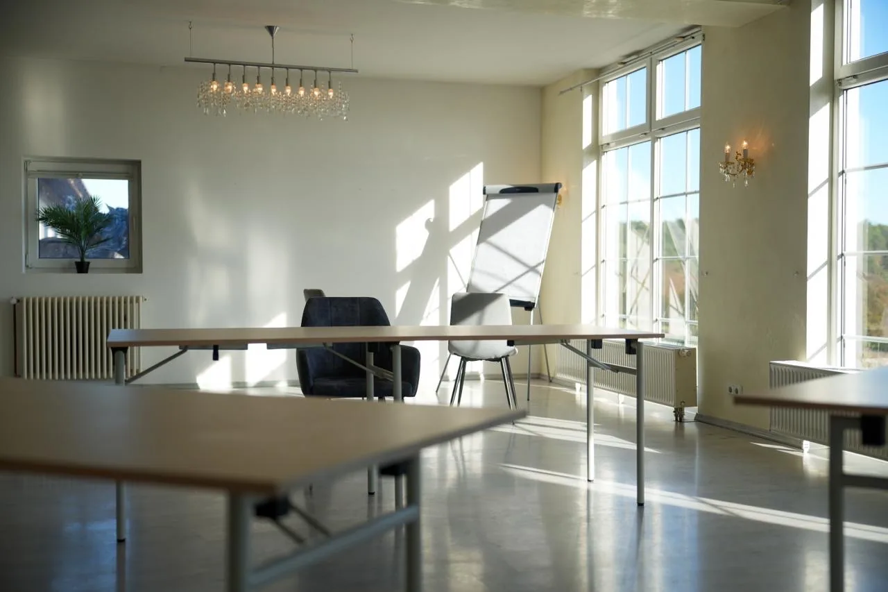 Salle de Pluvinel mit Tischen, Stühlen, Flipchart und Kristallkronleuchter, helles Tageslicht durch die Fensterfront