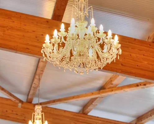 Kristallkronleuchter hängt zwischen hellen Holzbindern an der weißen Decke des Saals